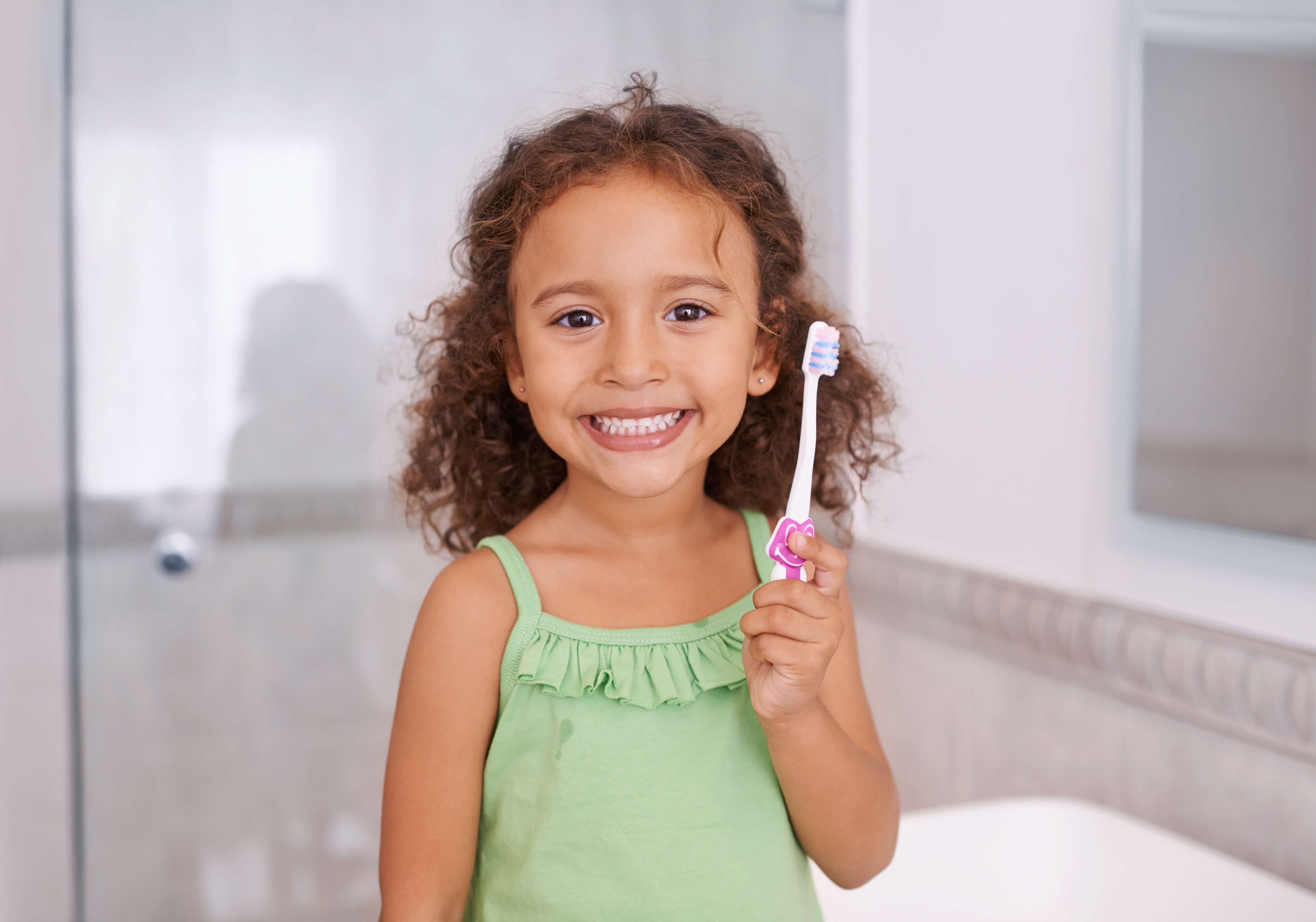 Child dressed in green holding a toothbrush smiling.